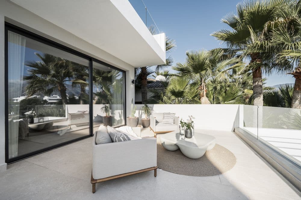 Living room with sofas opening onto a terrace with palm-lined view through sliding glass doors