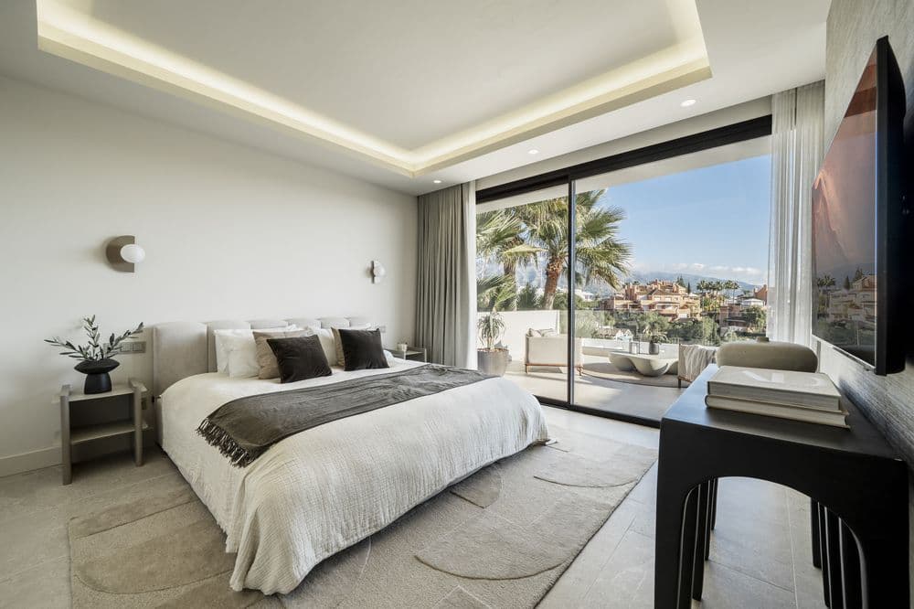 Bedroom with bed facing glass doors open to a view, desk and TV