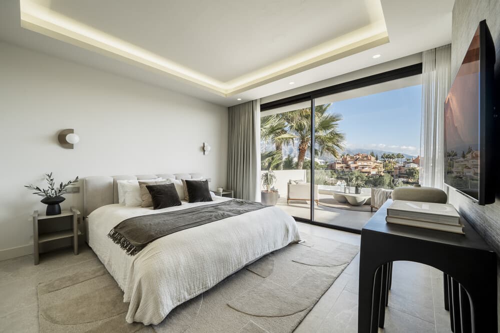 Habitación con la cama frente a puertas de vidrio abiertas hacia la vista, con escritorio y televisor