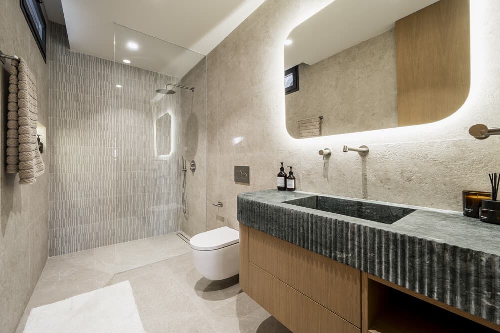 Baño con ducha de entrada directa, lavamanos con encimera de piedra y espejo retroiluminado