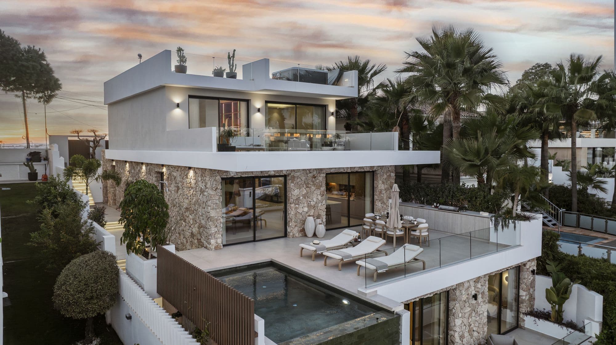 Twilight exterior view of the villa with pool and stone facade lit up