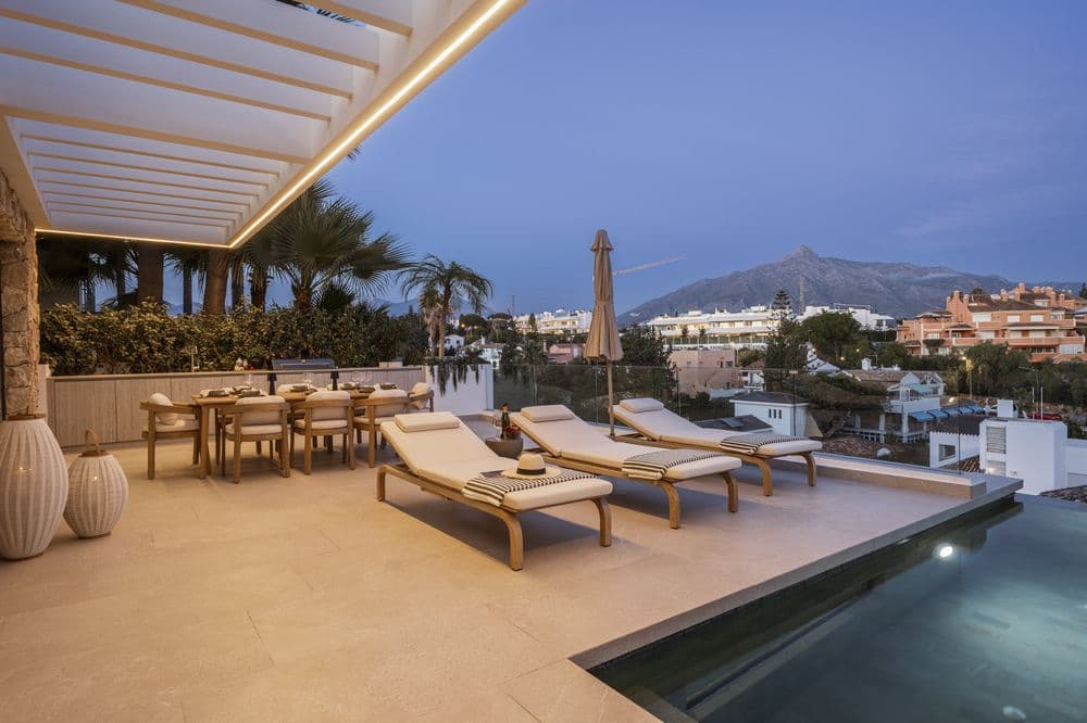 Twilight pool terrace with pergola, dining set and illuminated pool overlooking the valley
