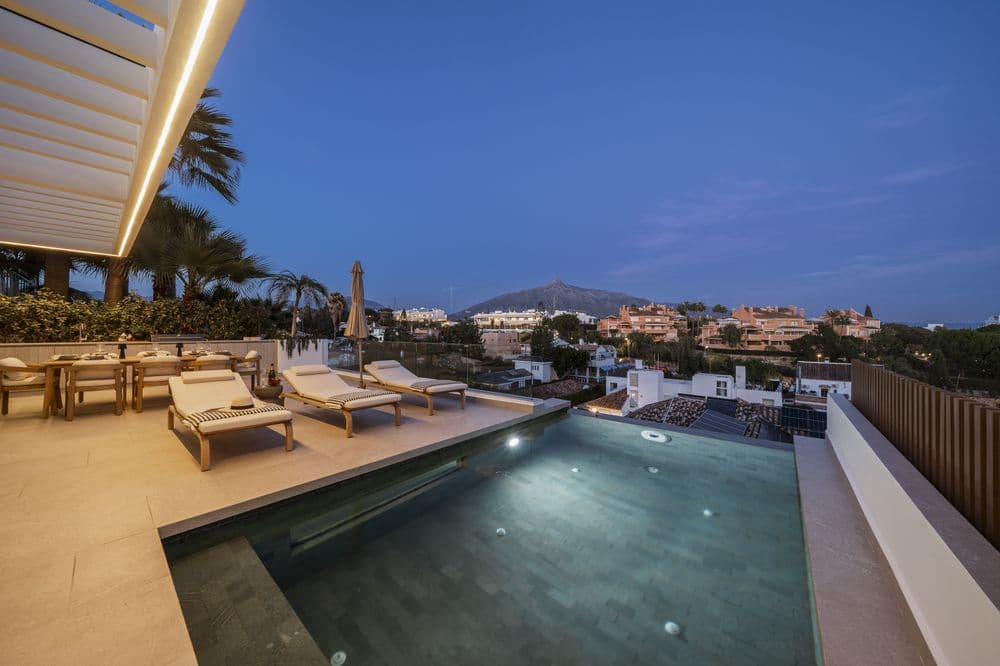 Twilight infinity pool with loungers, pergola shadow and mountain silhouette
